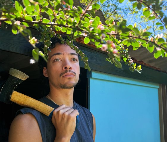 Aurel Mertz in ärmellosem T-Shirt und ein Beil in der Hand, das er über die Schulter gelegt hat.