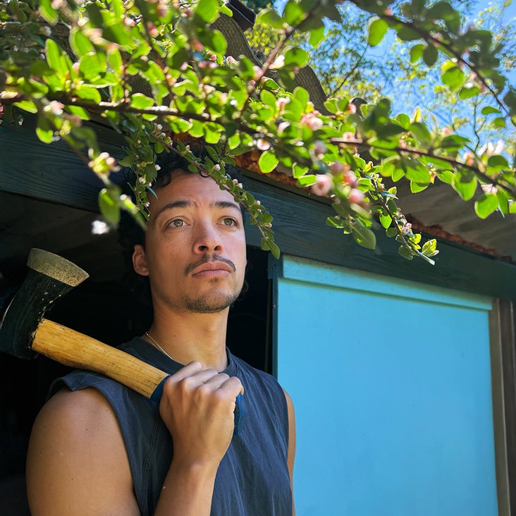 Aurel Mertz in ärmellosem T-Shirt und ein Beil in der Hand, das er über die Schulter gelegt hat.
