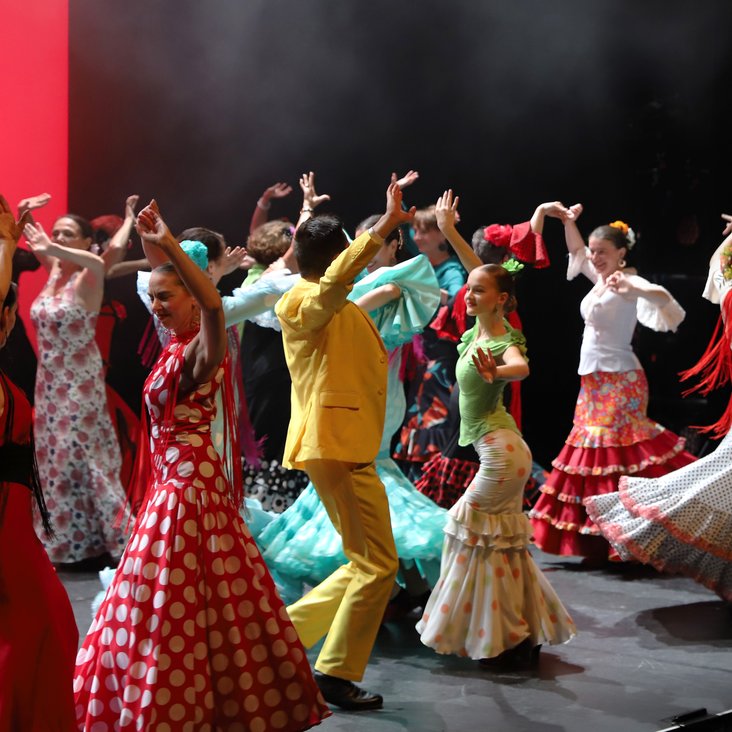 Mehrere Flamencotänzer:innen in bunten Kleidern auf einer Bühne, wie sie tanzen