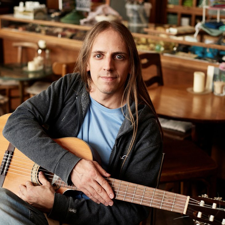 Portraitfoto des Musikers Weiherer, es zeigt ihn mit Gitarre in einer Bar oder Kneipe.