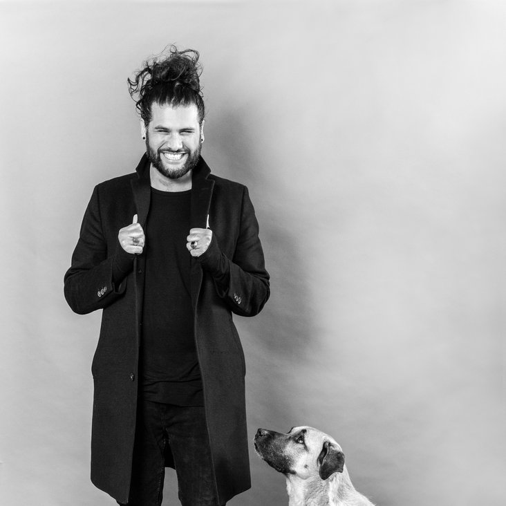 Masih Samin steht lächelnd neben einen Hund der neben ihm sitzt und ihn anschaut