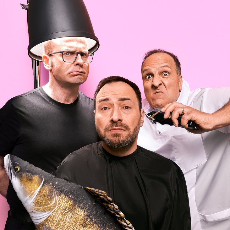 Drei Männer vor einem rosa Hintergrund, einer ist unter einer Frisörhaube, der andere hat einen Fisch in der Hand