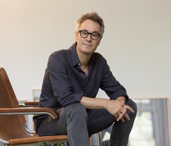 Porträt eines Komponisten im Sitzen in einem hellen Raum, entspannte, nachdenkliche Haltung.