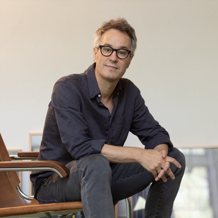 Porträt eines Komponisten im Sitzen in einem hellen Raum, entspannte, nachdenkliche Haltung.