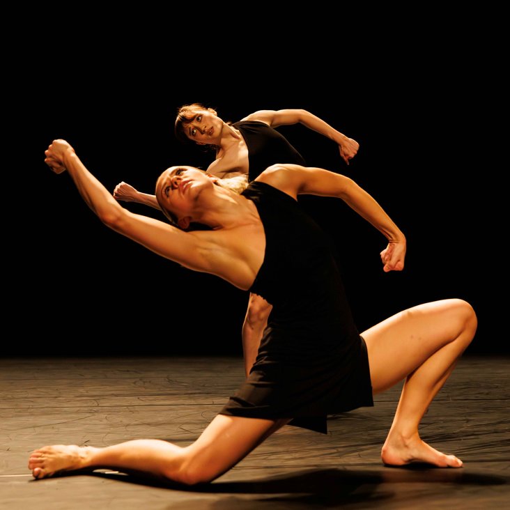 Tänzer:innen in Kostüm auf der Bühne, der Boden ist schwarz und die Bühne ist professionell ausgeleuchtet.