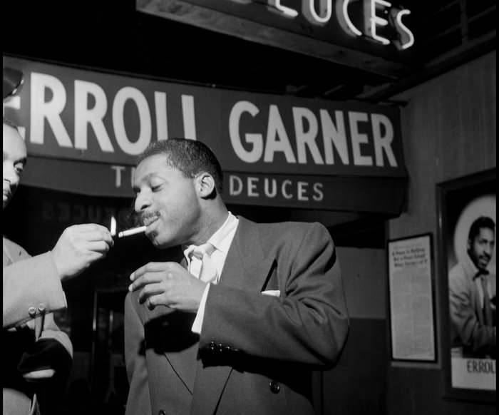 Der Pianist Erroll Garner steht in einer Konzertlocation. Ihm wird eine Zigarette angezündet.