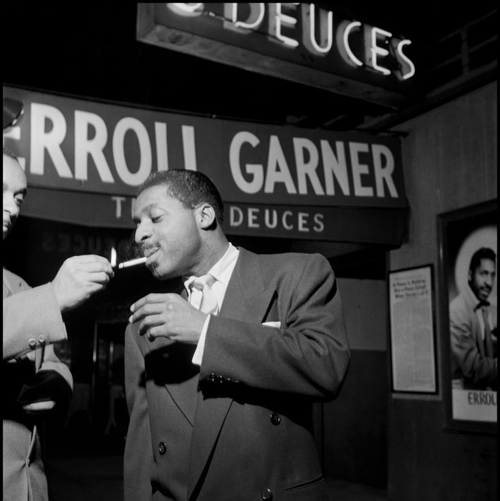 Der Pianist Erroll Garner steht in einer Konzertlocation. Ihm wird eine Zigarette angezündet.
