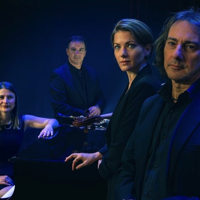 Das Quartett schaut in die Kamera, der Hintergrund ist schwarz und die Beleuchtung blau.