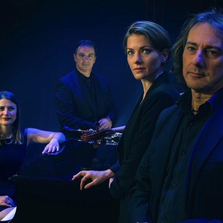 Das Quartett schaut in die Kamera, der Hintergrund ist schwarz und die Beleuchtung blau.