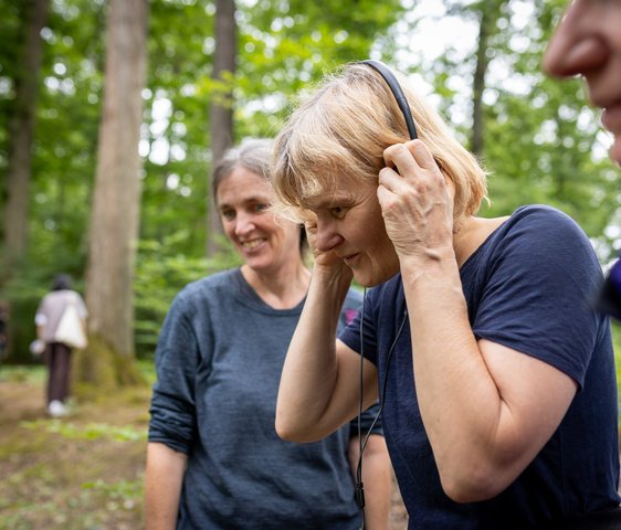 Teilnehmende einer Musikveranstaltung im Wald, Menschen hören Klängen über Kopfhörer in natürlicher Umgebung zu.