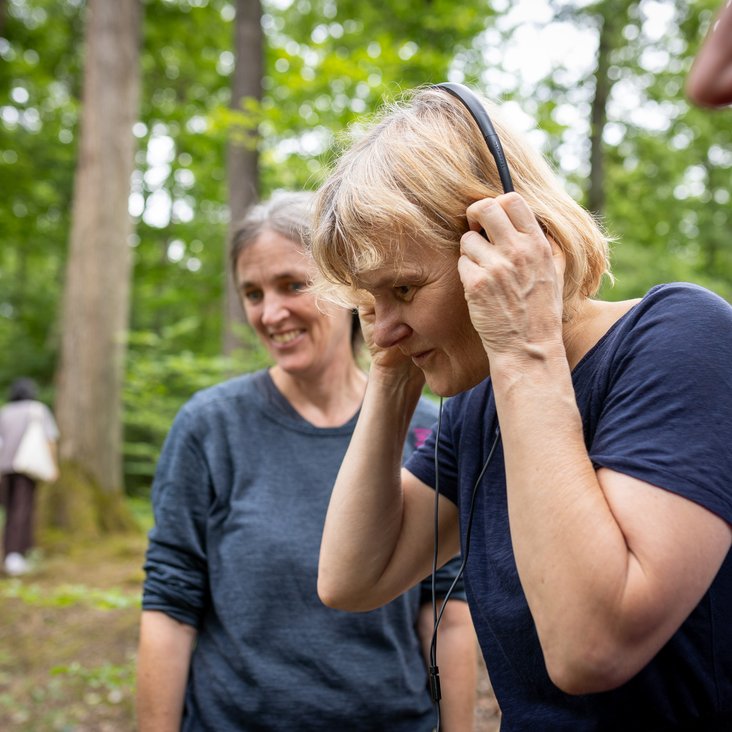 Teilnehmende einer Musikveranstaltung im Wald, Menschen hören Klängen über Kopfhörer in natürlicher Umgebung zu.