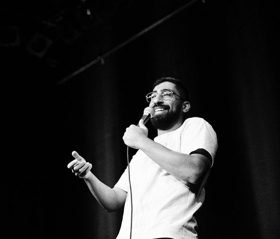 Ein schwarz-weiß Foto von Kawus Kalantar wie er ein Mikrofon in der Hand hält und auf einer Bühne steht.