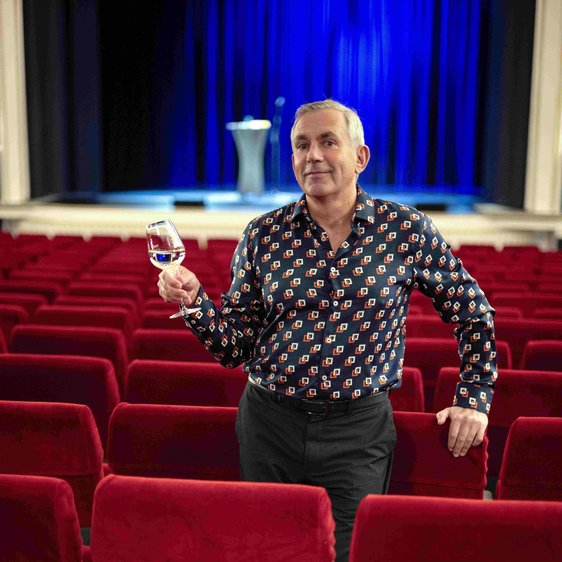 Wladimir Kaminer steht mit einem Weinglas in der Hand im Zuschauerraum eines Theaters