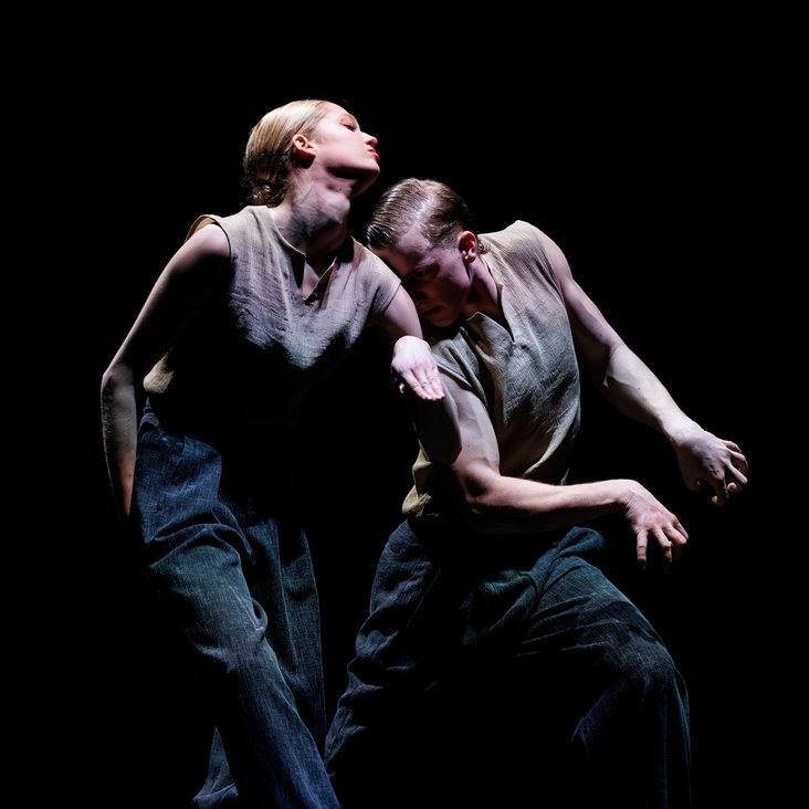 Tänzer:innen in Kostüm auf der Bühne, der Boden ist schwarz und die Bühne ist professionell ausgeleuchtet.