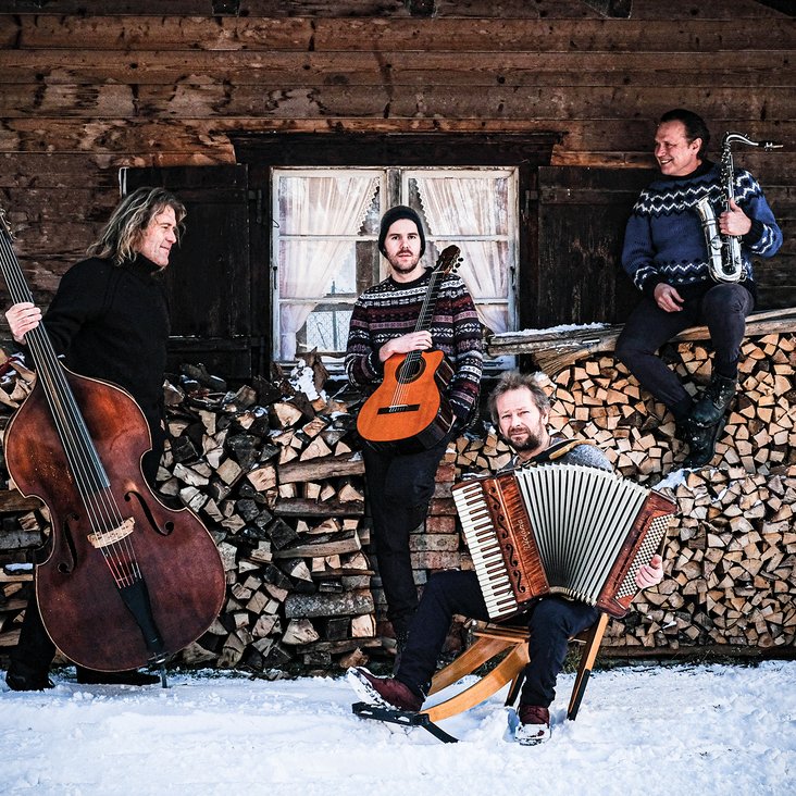 Die Musiker von Quadro Nuevo mit ihren Instrumenten im Schnee vor einer Hütte