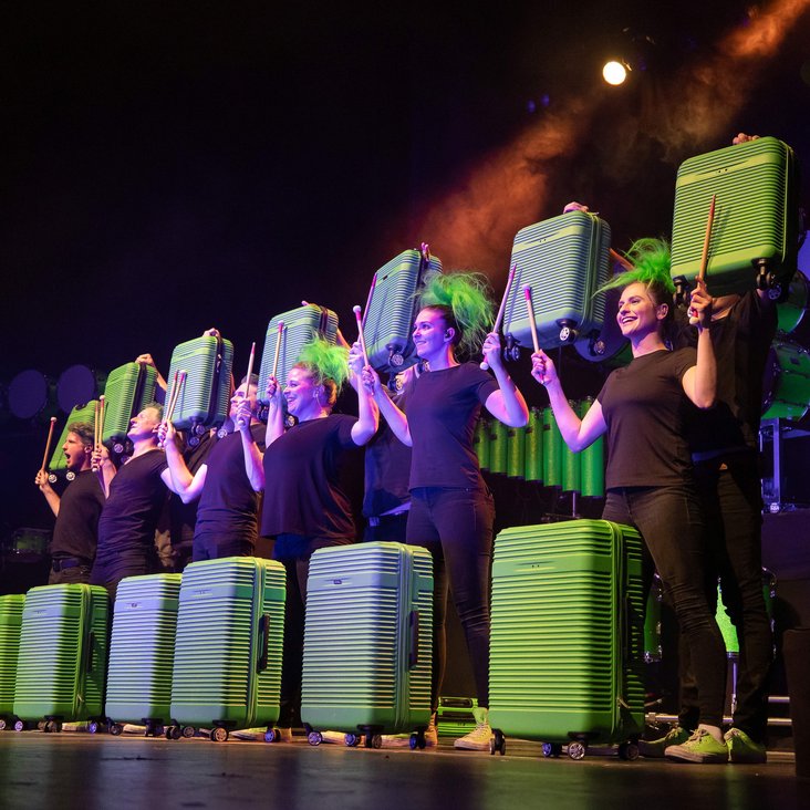 Das greenbeats Ensemble auf der Bühne, sie trommeln auf grünen Koffern.