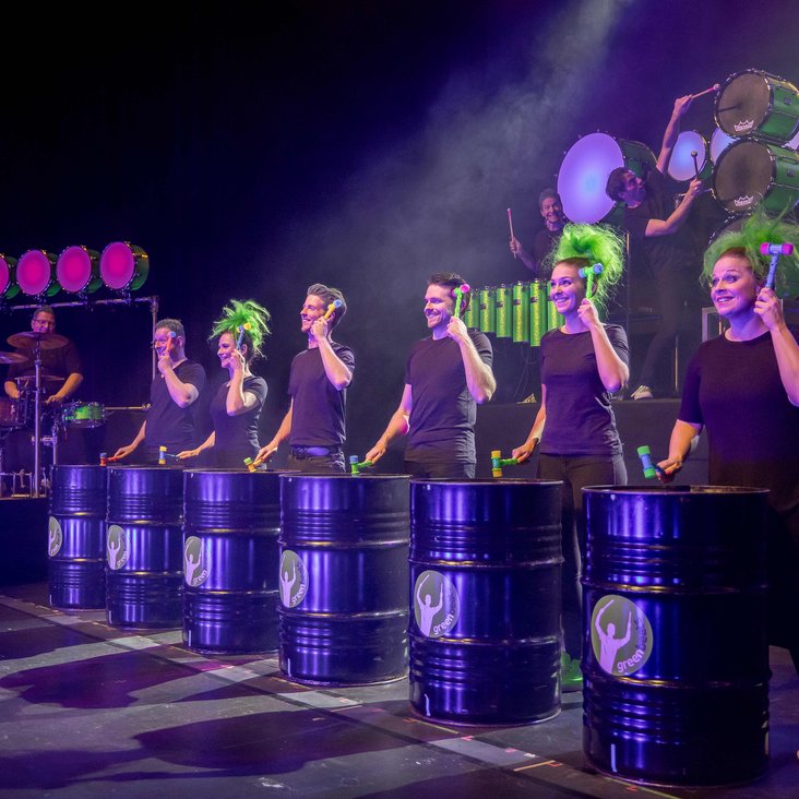 Das greenbeats Ensemble auf der Bühne: Mit grünen Perücken trommeln sie auf Tonnen.