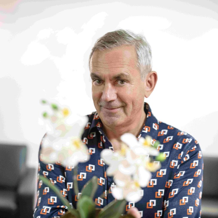 Wladimir Kaminer hält einen Blumentopf mit einer weißen Blume in Richtung der Kamera. Sein Gesicht ist scharf, der Blumentopf im Vordergrund verschwommen.