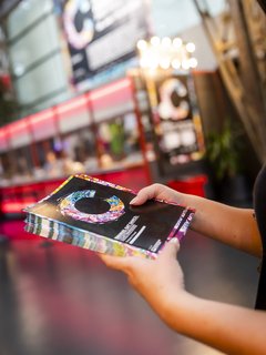 Im Theaterhaus Foyer. Das Foyer ist prächtig im Look des COLOURS International Dance Festivals. Zwei Hände halten einen Stapel Programmflyer.