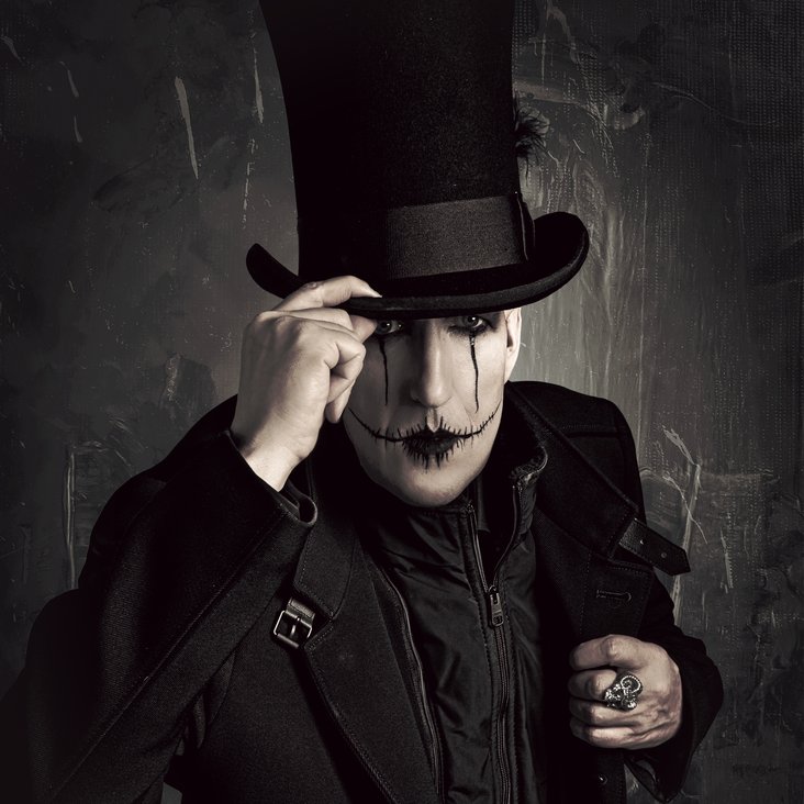 Ein düster geschminkter Mann im Gothic-Look fasst sich an seinen Zylinder.