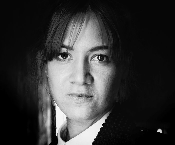Ein schwarz weiß Portrait einer Frau. Sie trägt eine weiße Bluse, Strähnen eines leichten Ponys fallen ihr ins Gesicht.