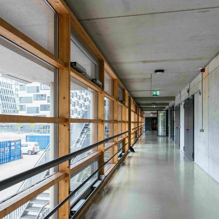 Langer Flur mit Fenstern und Geländer entlang der Glasfront.
