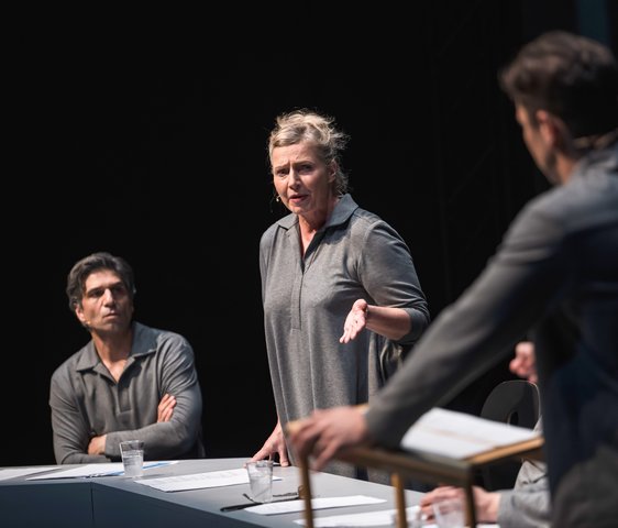 Szenenfoto, es zeigt drei Schauspieler:innen, die grau gekleidet sind, auf der Bühne