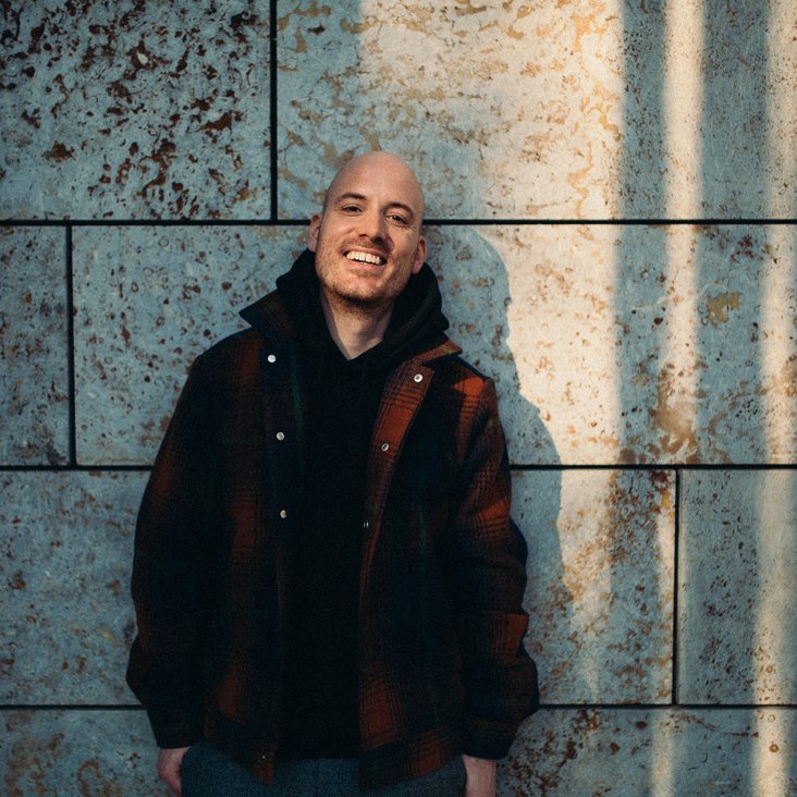 Lars Amend lehnt an eine Wand und lacht