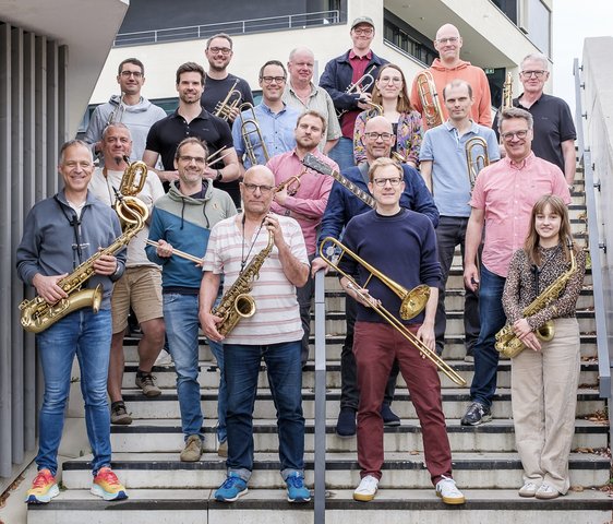 Gruppenfoto der mitteBIGband, die Mitglieder stehen auf einer Treppe, einige haben ihre Instrumente in der Hand.