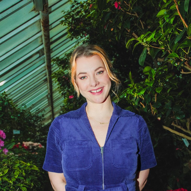 Portraitfoto von Kristina Bogansky, sie trägt einen blauen Kurzarm-Anzug und blickt in die Kamera.