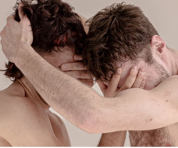 Zwei Tänzer halten sich die Augen zu und sind einander zugewandt.