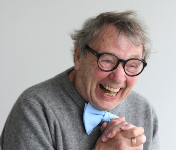 Portraitfoto von Peter Grohmann, er trägt einen grauen Pullover, eine Brille mit dunklem breiten Rahmen und eine hellblaue Fliege