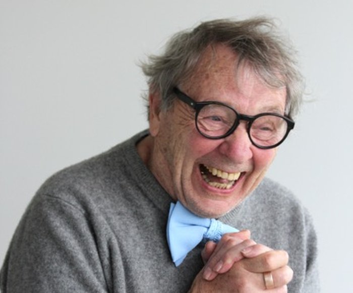 Portraitfoto von Peter Grohmann, er trägt einen grauen Pullover, eine Brille mit dunklem breiten Rahmen und eine hellblaue Fliege
