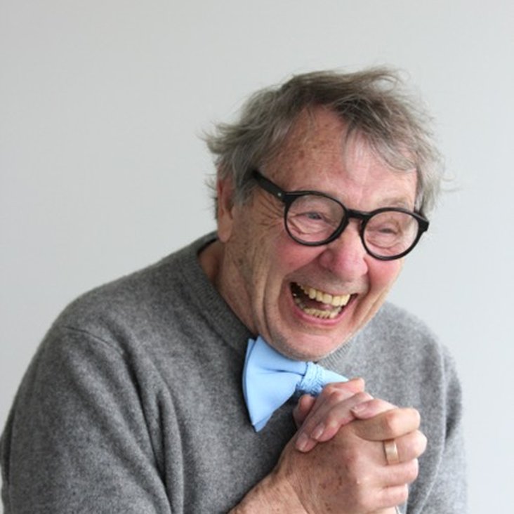 Portraitfoto von Peter Grohmann, er trägt einen grauen Pullover, eine Brille mit dunklem breiten Rahmen und eine hellblaue Fliege