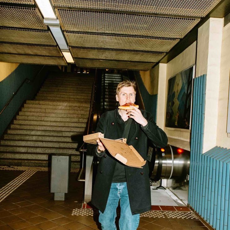 Till Reiner läuft mit einem Pizzakarton in einer Unterführung auf die Kamera zu und beißt dabei in ein Stück Pizza