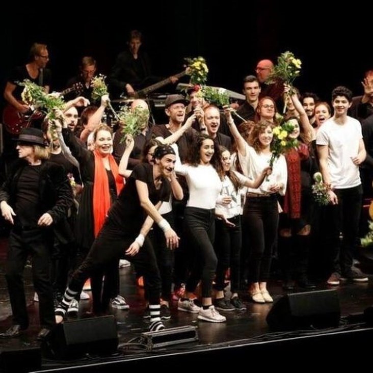 Eine Gruppe an Künstler:innen verteilt Blumen auf einer Bühne.