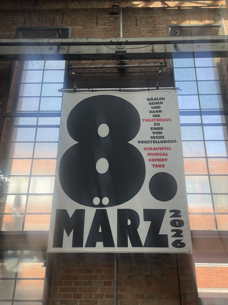 Ein Plakat das im Foyer des Theaterhauses hängt. In großen Buchstaben steht "8. März 2026" darauf, daneben: Wählen gehen und dann ins Theaterhaus zu einer von sechs Vorstellungen. Schauspiel, Musical, Comedy, Tanz