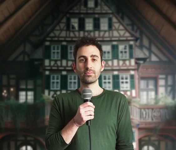 Fabi Rommel steht vor einem Hintergrund mit Fachwerkhäusern, in der Hand hält er ein Mikrofon