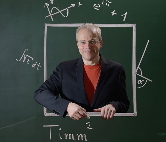 Timm Sigg steht vor einem Layout einer Kreidetafel mit Beschriftungen mathematischer Formeln