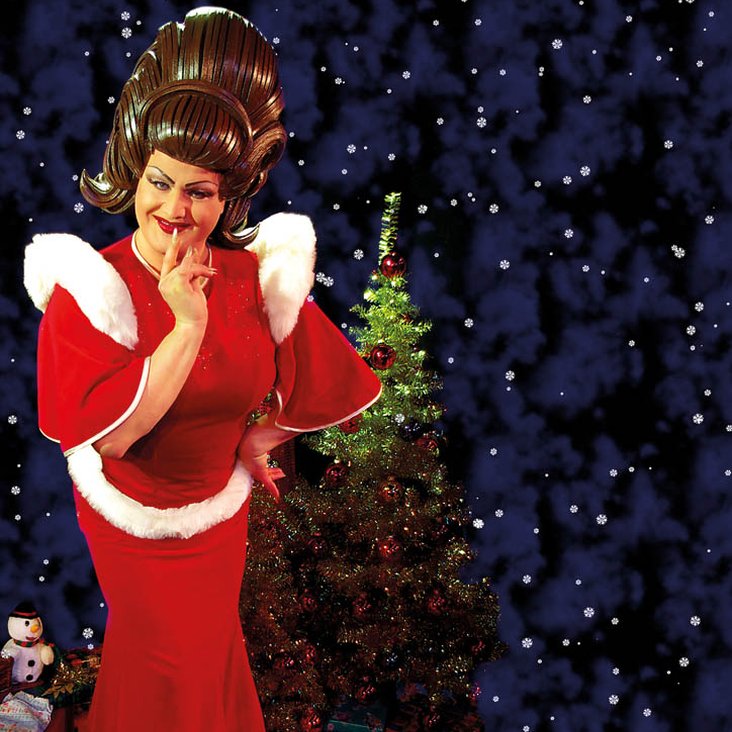 Die Künstler:in steht schmunzelnd vor einem Weihnachtsbaum