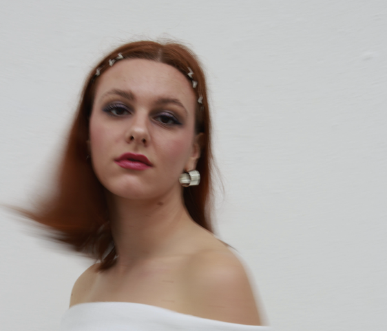 Portraitfoto von Katharina Göppert, sie trägt ein weißes Oberteil und kinnlanges rotes Haar. Sie blickt in die Kamera.