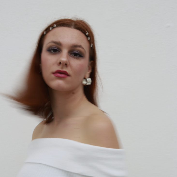 Portraitfoto von Katharina Göppert, sie trägt ein weißes Oberteil und kinnlanges rotes Haar. Sie blickt in die Kamera.