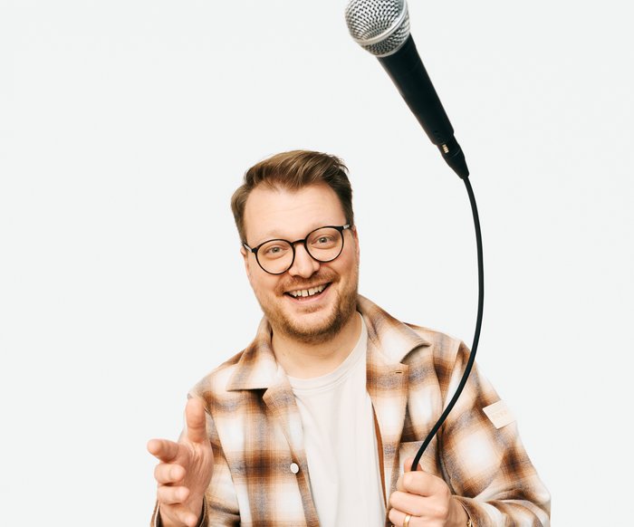 Auf dem Foto ist Maxi Gstettenbauer zu sehen. Er trägt ein kariertes Hemd und wirft ein Mikrofon in die Luft.