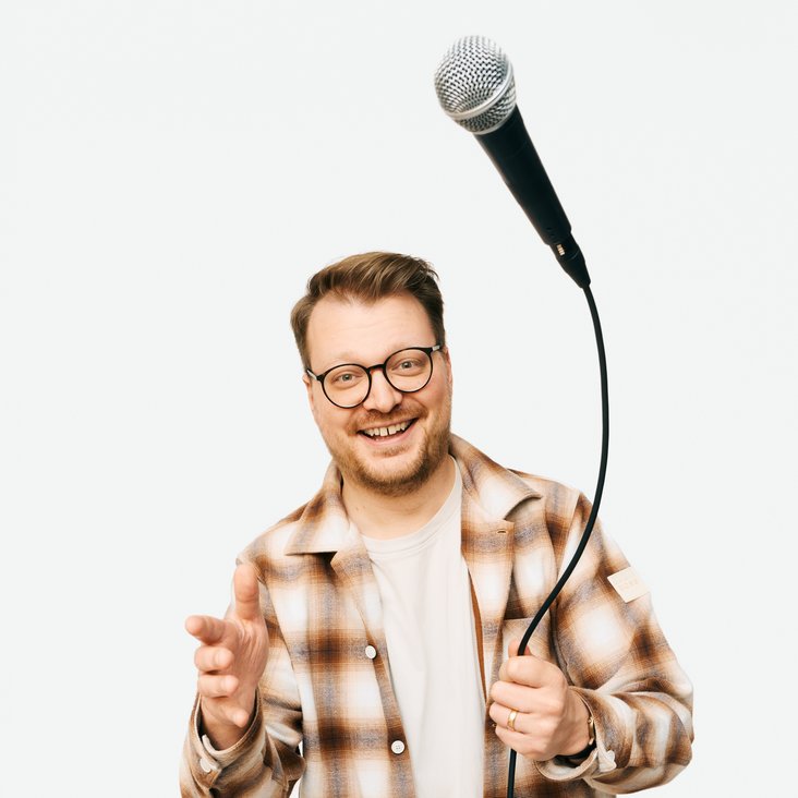 Auf dem Foto ist Maxi Gstettenbauer zu sehen. Er trägt ein kariertes Hemd und wirft ein Mikrofon in die Luft.