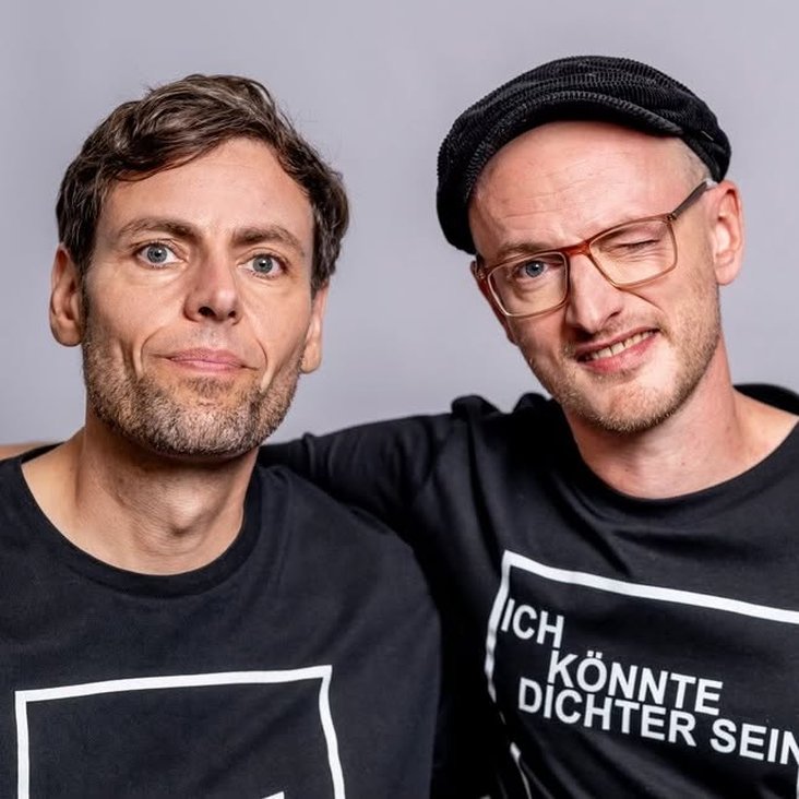 Portraitfoto der Künstler Simon & Jan, sie tragen schwarze T-Shirts mit der Aufschrift "ICH KÖNNTE DICHTER SEIN".