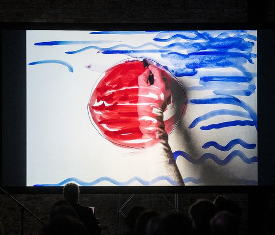 Videoprojektion mit grafischen Elementen und rotem Kreis in einer dunklen Ausstellungs- oder Bühnenumgebung.