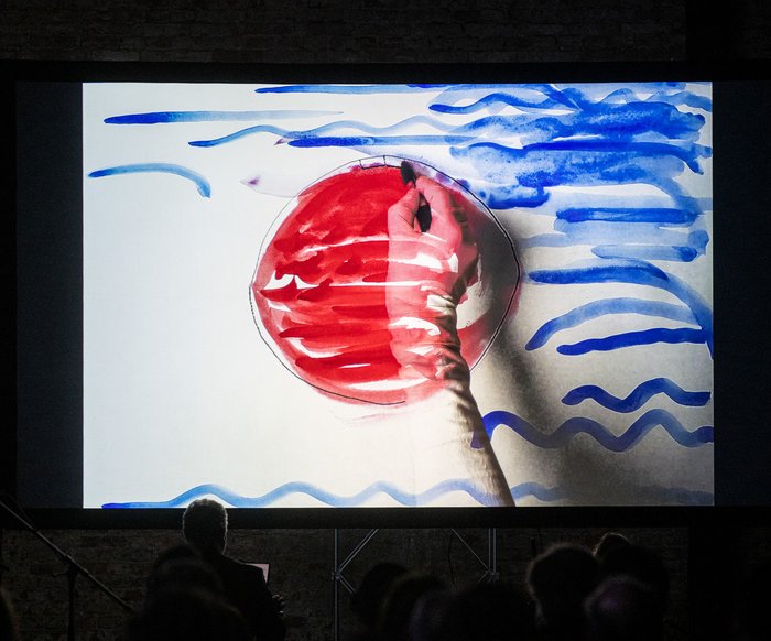 Videoprojektion mit grafischen Elementen und rotem Kreis in einer dunklen Ausstellungs- oder Bühnenumgebung.