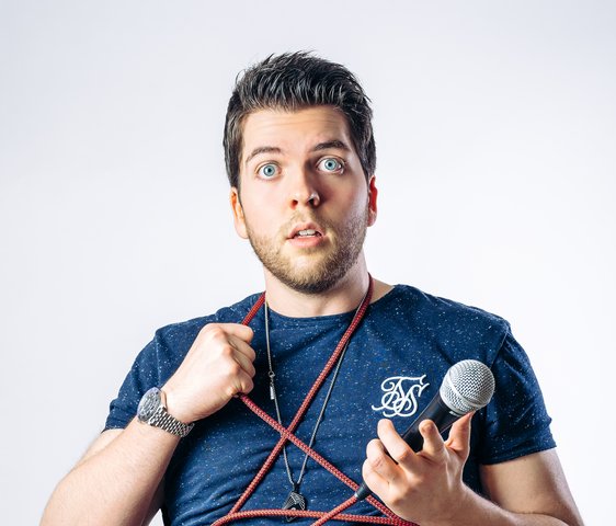 Alexander Straub guckt fragend in die Kamera, er ist eingewickelt in das Kabel seines Mikrofons