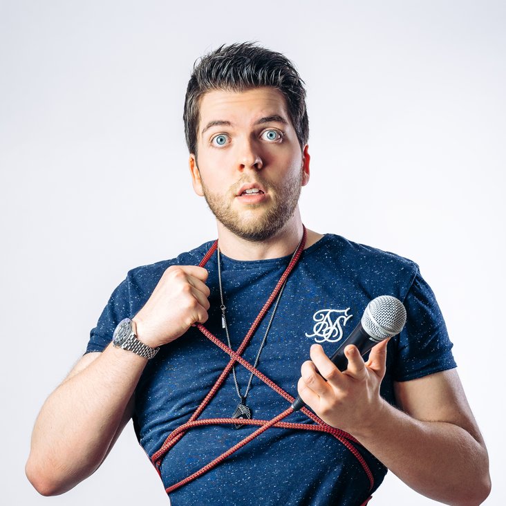 Alexander Straub guckt fragend in die Kamera, er ist eingewickelt in das Kabel seines Mikrofons