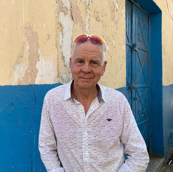 Matthias Politycki steht vor einer blauen Wand. Er hat graues Haar und trägt lässig eine rote Sonnenbrille auf dem Kopf.